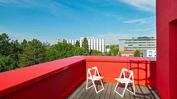 Roter Balkon mit einem Tisch und zwei Stühlen; Aussicht über die Stadt